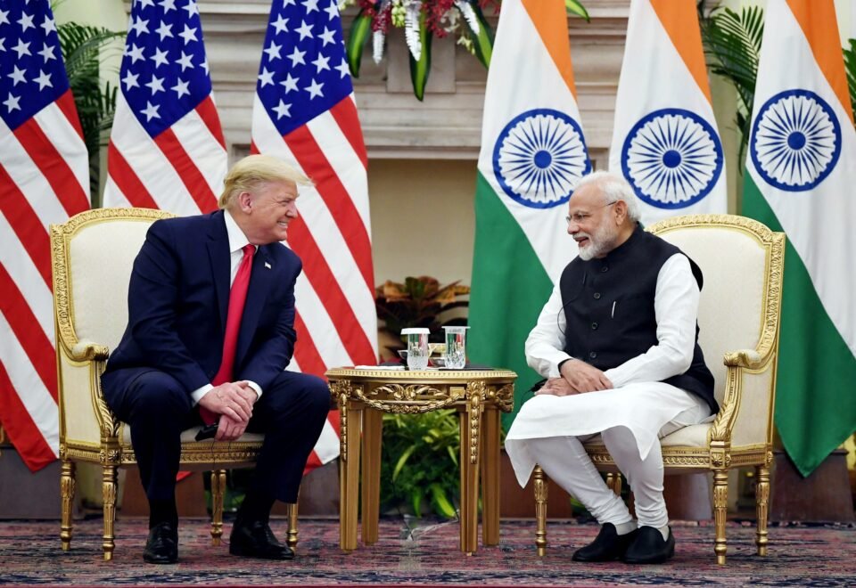 "Donald Trump and Narendra Modi shaking hands during a diplomatic meeting with U.S. and Indian flags in the background."
