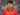 Son Heung-min wearing a red South Korean football jersey, standing on the field with a focused expression and a blurred stadium background.