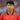Son Heung-min wearing a red South Korean football jersey, standing on the field with a focused expression and a blurred stadium background.