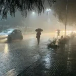 "Flooded streets in a Rajasthani town during heavy monsoon rainfall, with cloudy skies, waterlogged roads, and traditional buildings in the background."